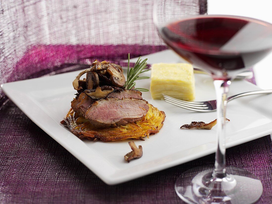 Beef fillet on rösti with mushrooms, glass of red wine