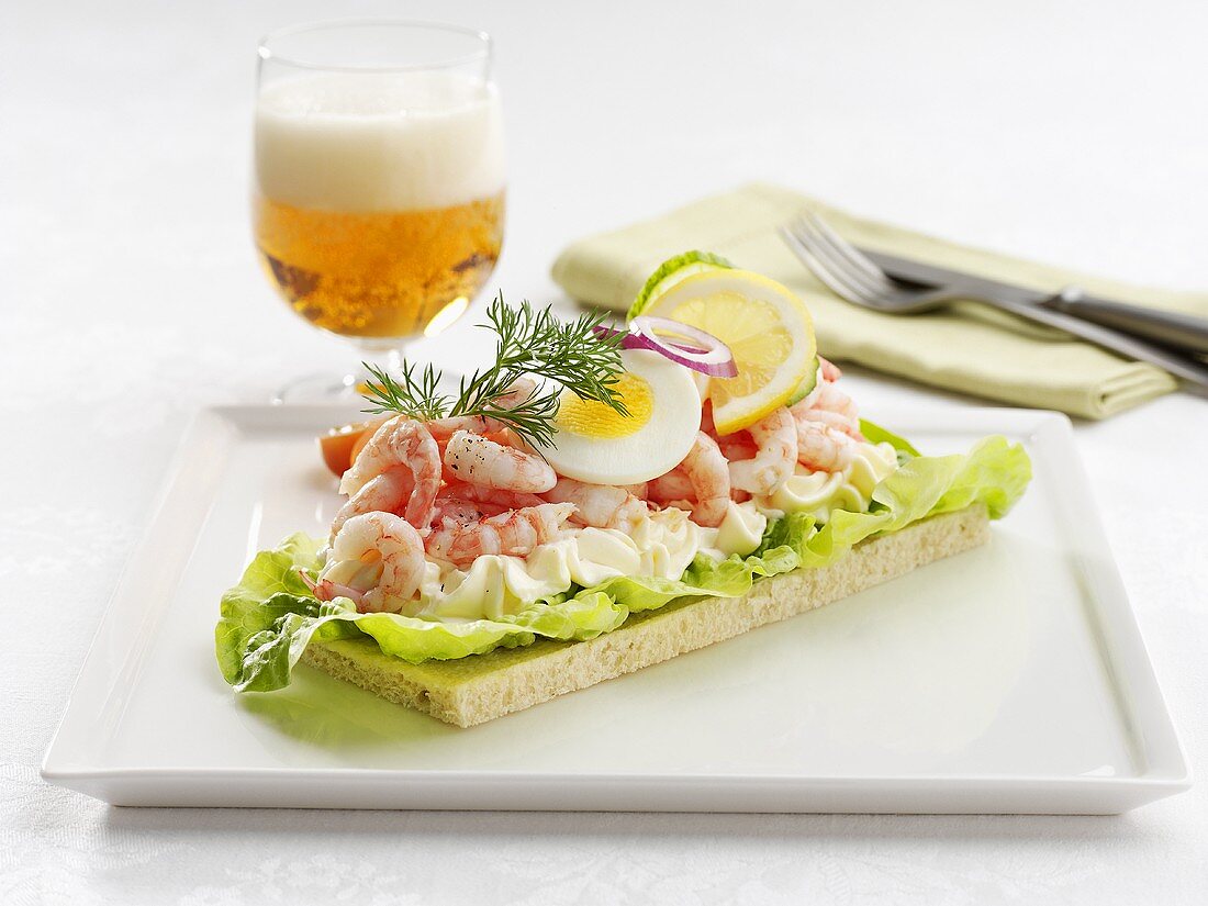 Shrimp and egg open sandwich with dill, glass of beer