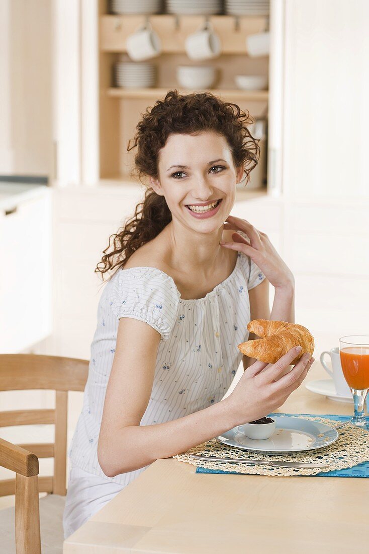 Young woman eating croissant for breakfast