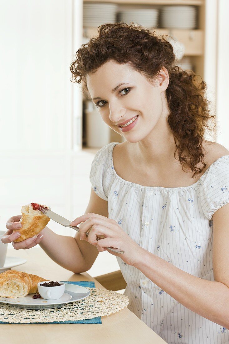 Young woman eating croissant with jam for breakfast