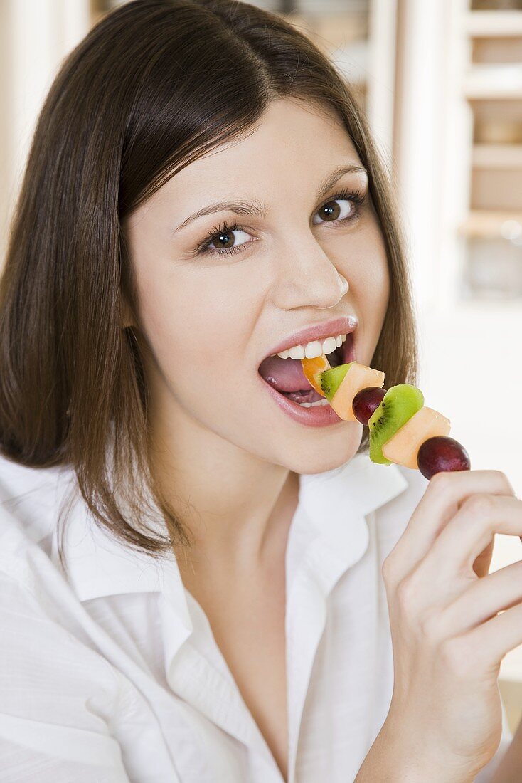 Young woman eating fruit skewer