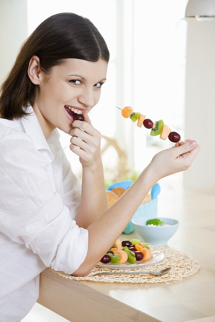 Young woman eating fruit skewer