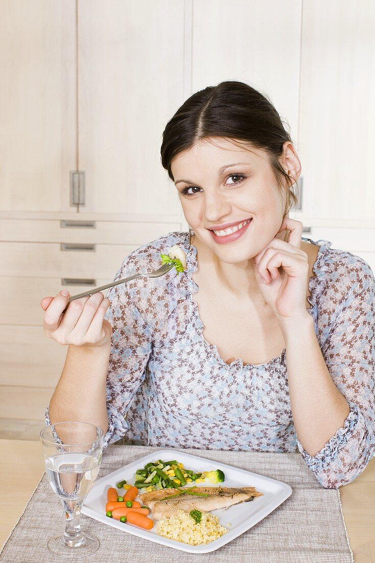 Young woman eating fish with couscous and vegetables