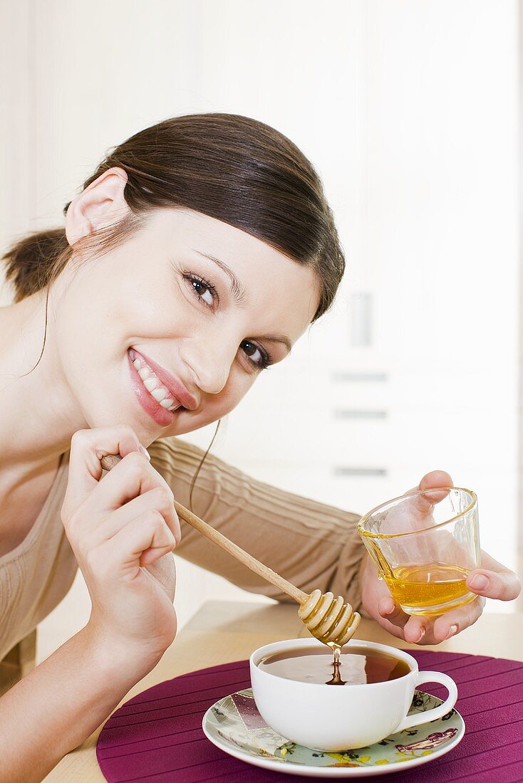 Junge Frau süsst ihren Tee mit Honig