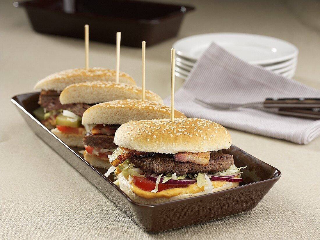 Four hamburger halves with bacon in a row