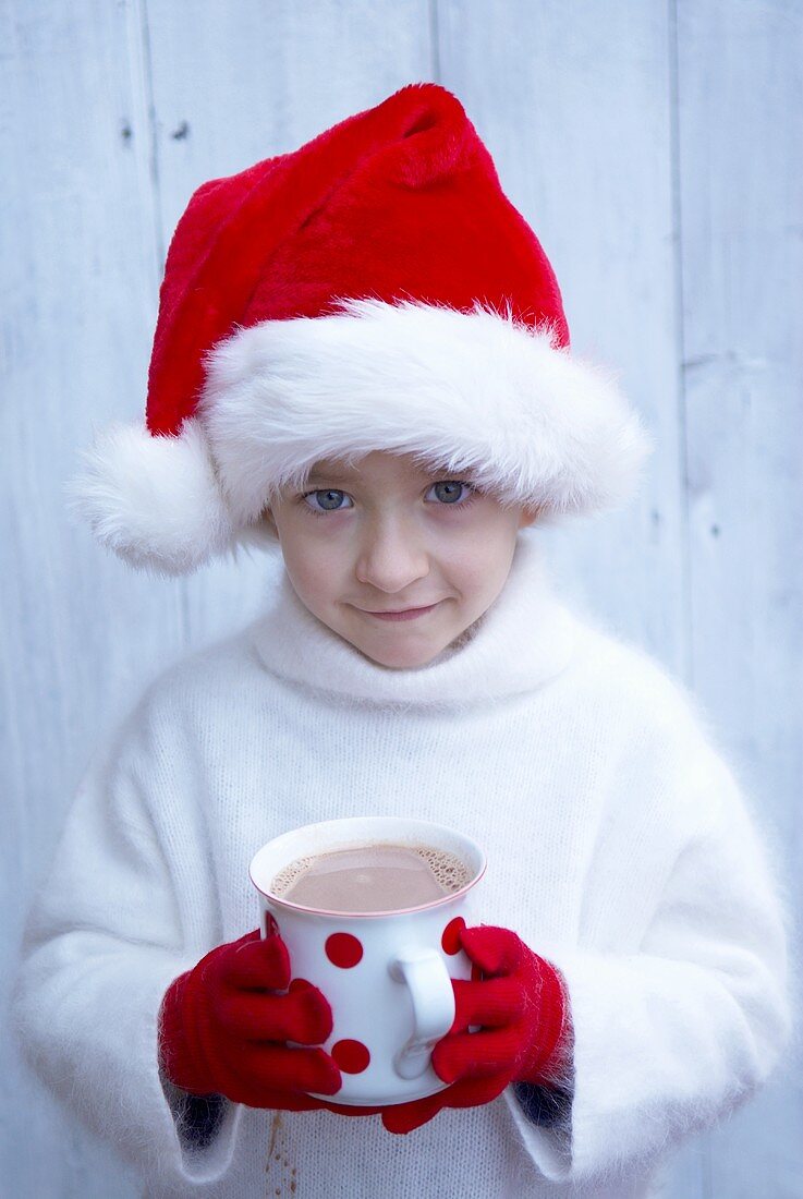 Kleiner Junge mit Nikolausmütze hält eine Tasse heiße Schokolade