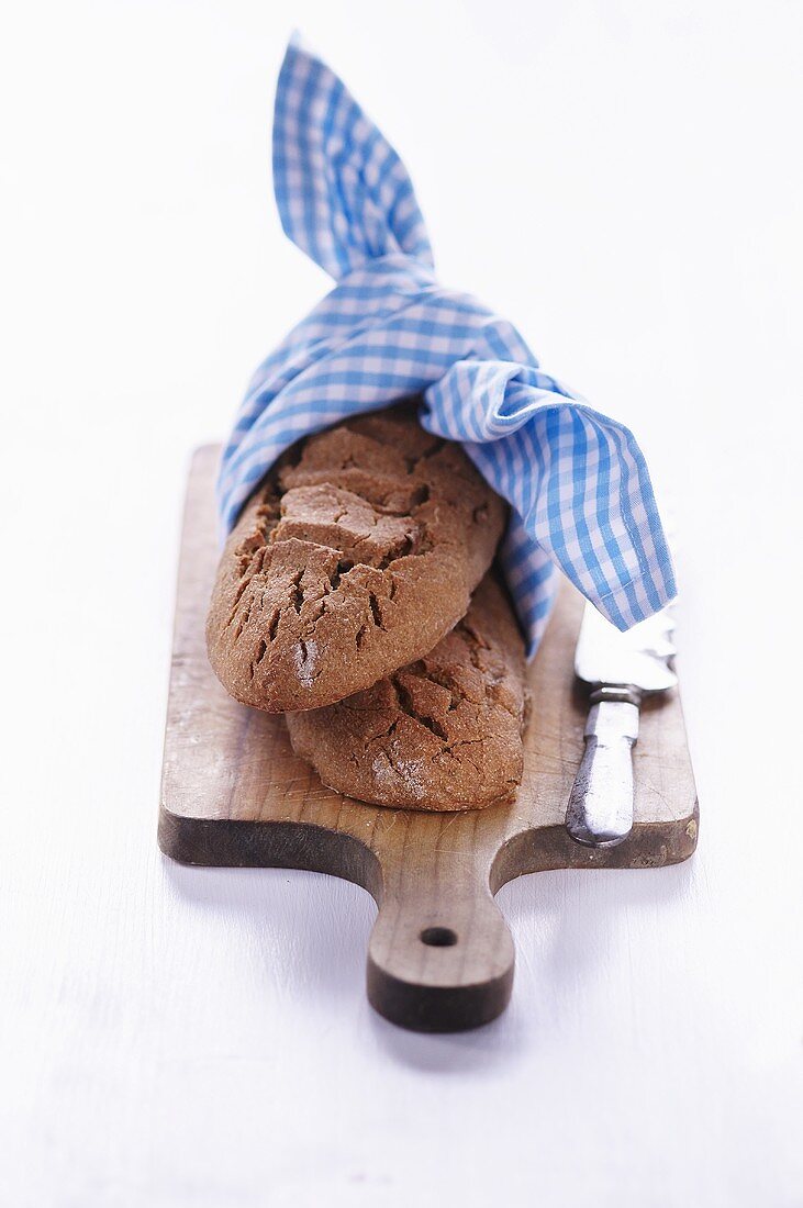 Zwei Brote mit blau-weißem Tuch auf Holzbrett
