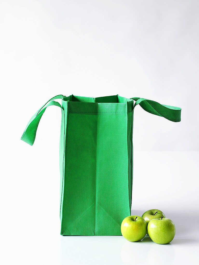 Three Granny Smith apples with a green shopping bag