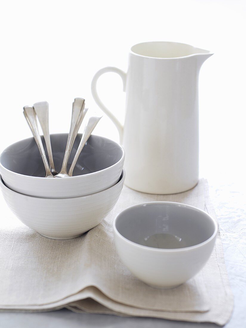 Porcelain bowls, jug and spoons on fabric napkin