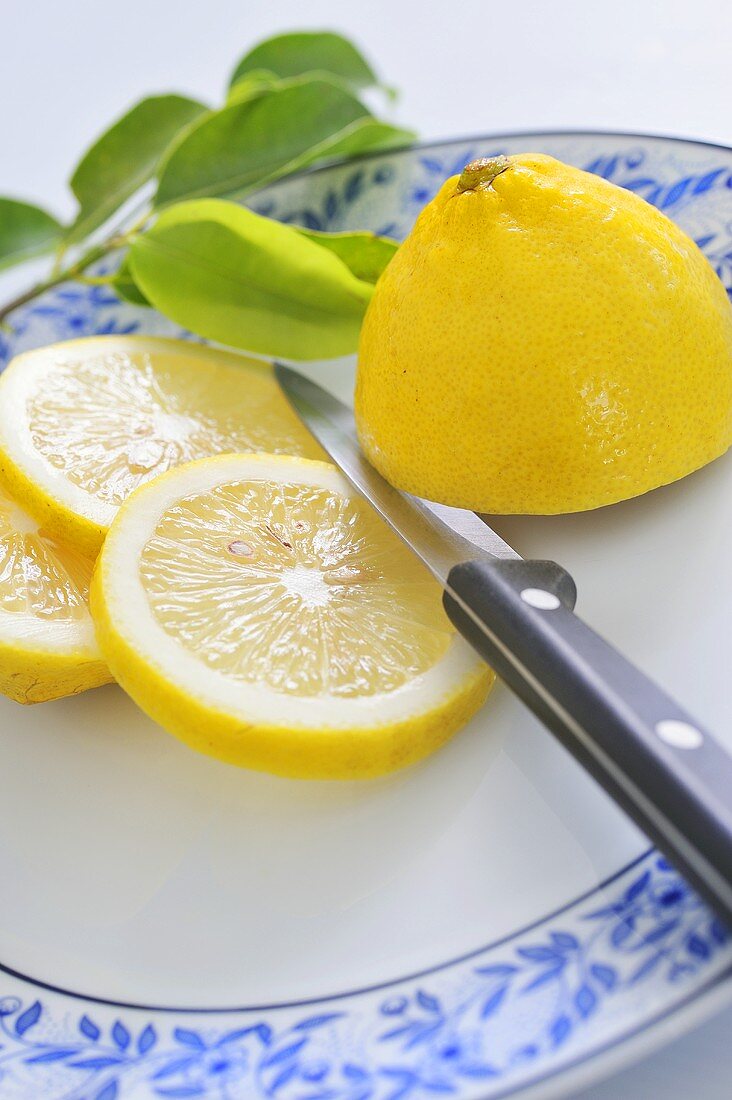 Half a lemon and lemon slices on plate with knife