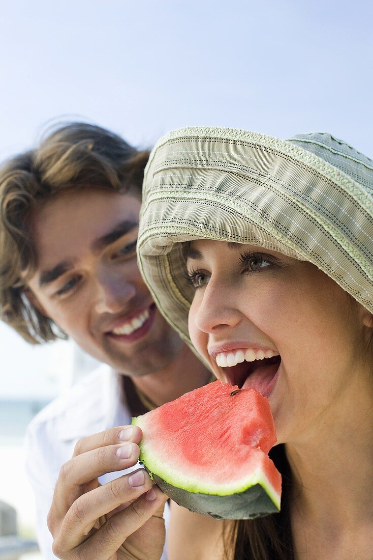 Young couple eating watermelon on beach