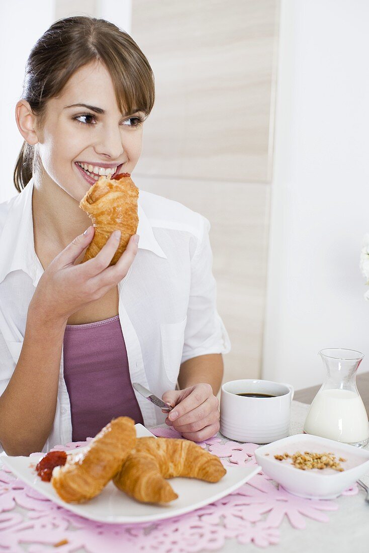 Young woman eating a croissant for breakfast