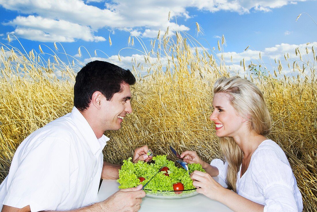 Young couple eating salad in a cornfield