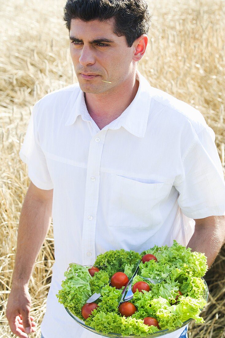 Young man with a bowl of salad in a cornfield