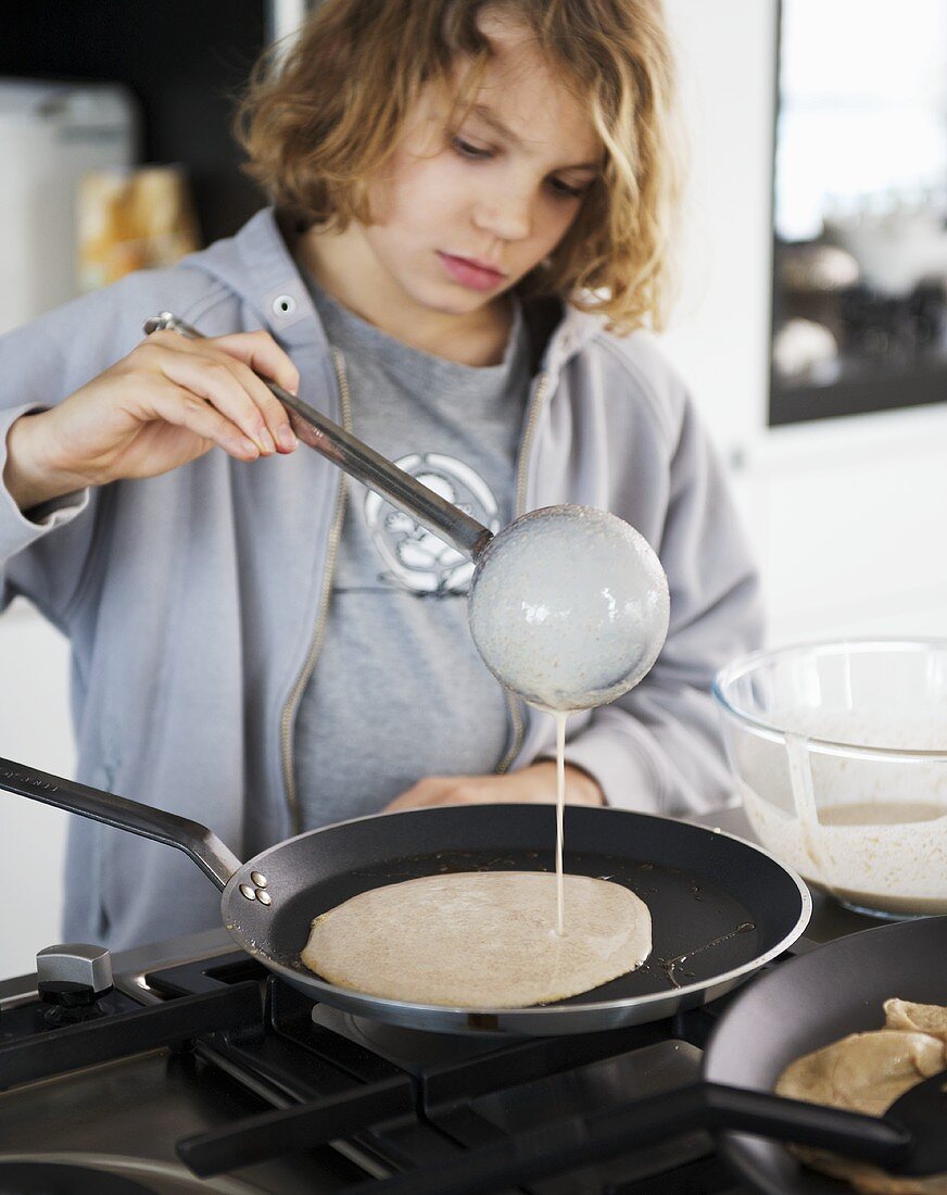 Boy putting pancake mixture into frying pan