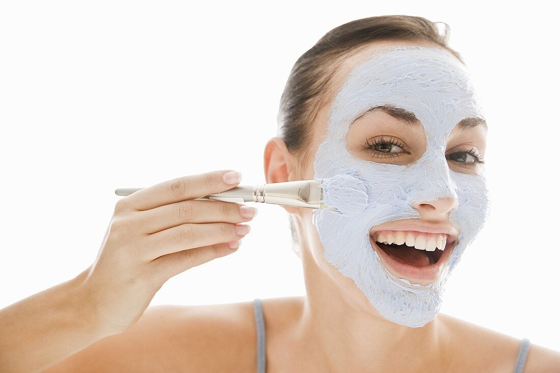 Young woman applying blue facial mask with brush