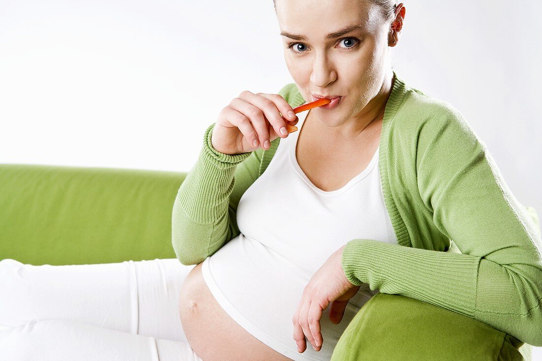 Schwangere Frau isst eine Möhre