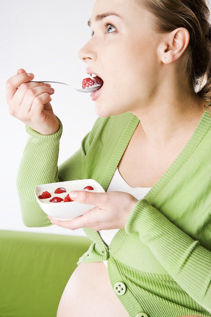 Pregnant woman eating yoghurt with raspberries
