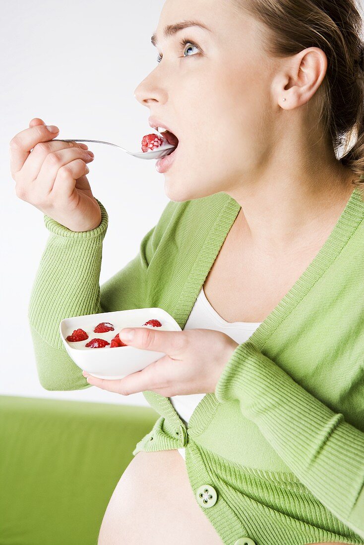 Schwangere Frau isst Joghurt mit Himbeeren