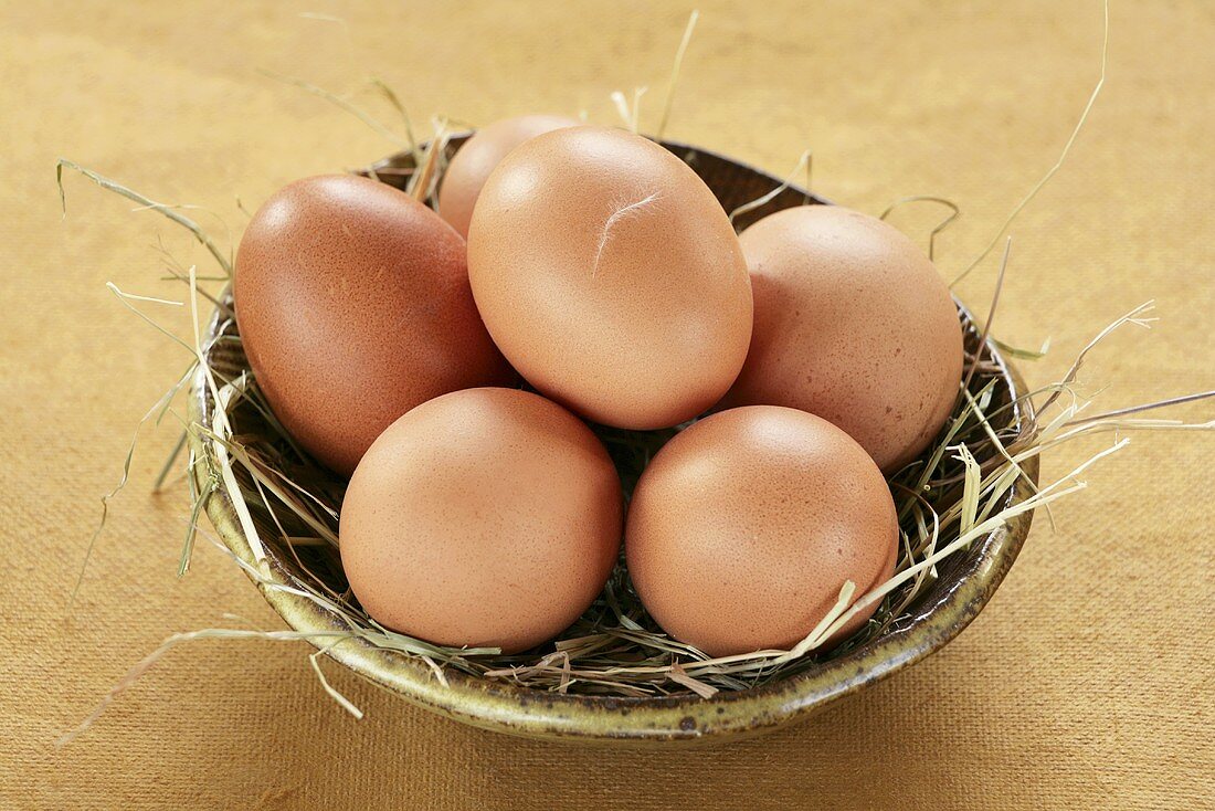 Braune Eier auf Heu in Keramikschale