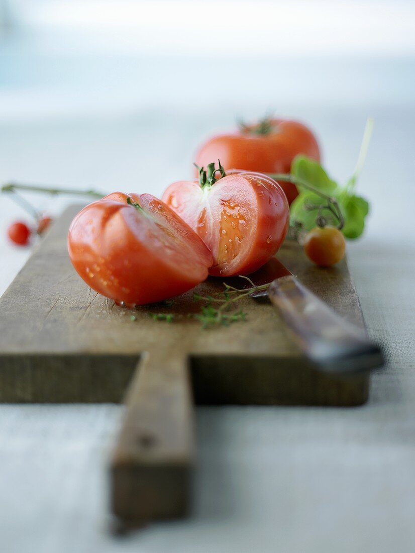 Ganze und halbierte Fleischtomate auf einem Schneidebrett