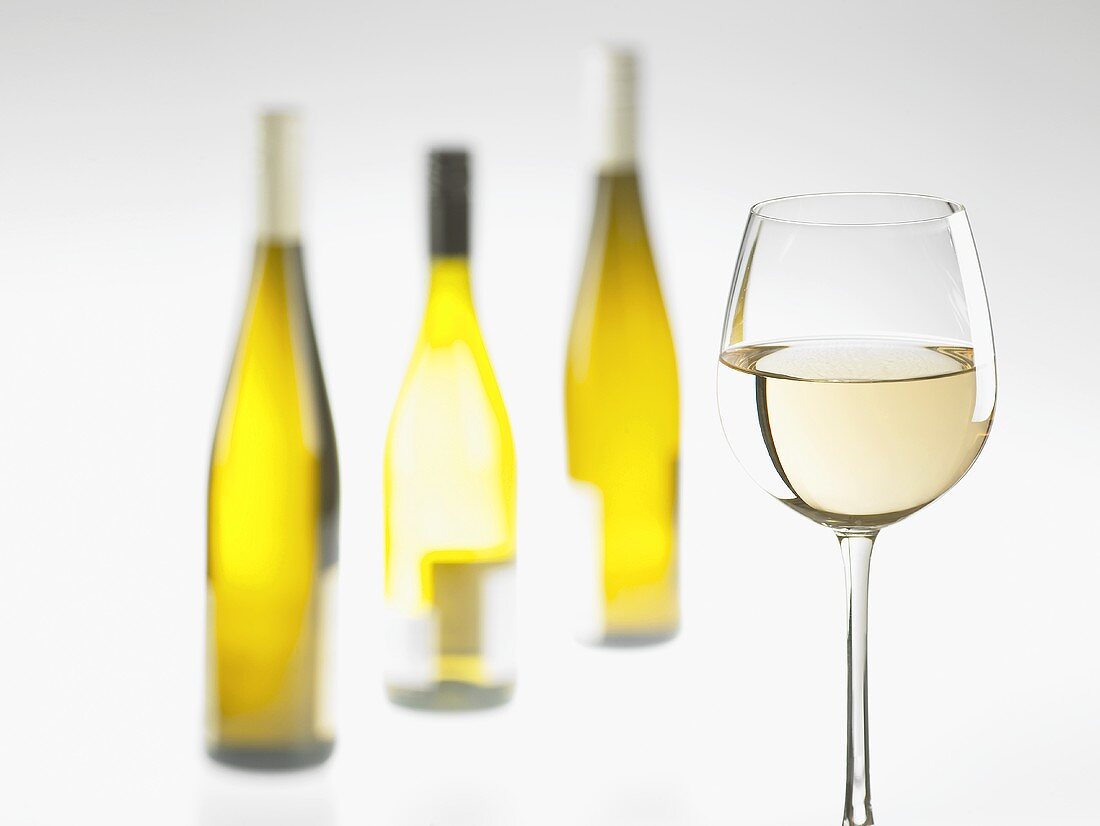 A glass and three bottles of white wine