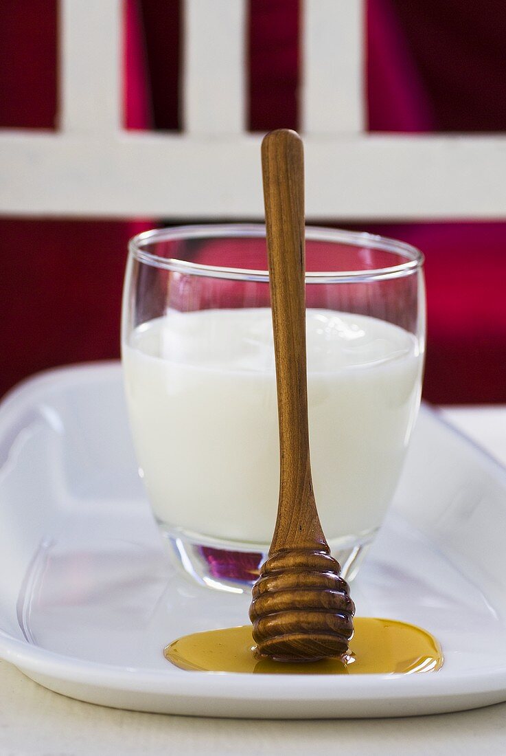 Glas Milch mit Honiglöffel