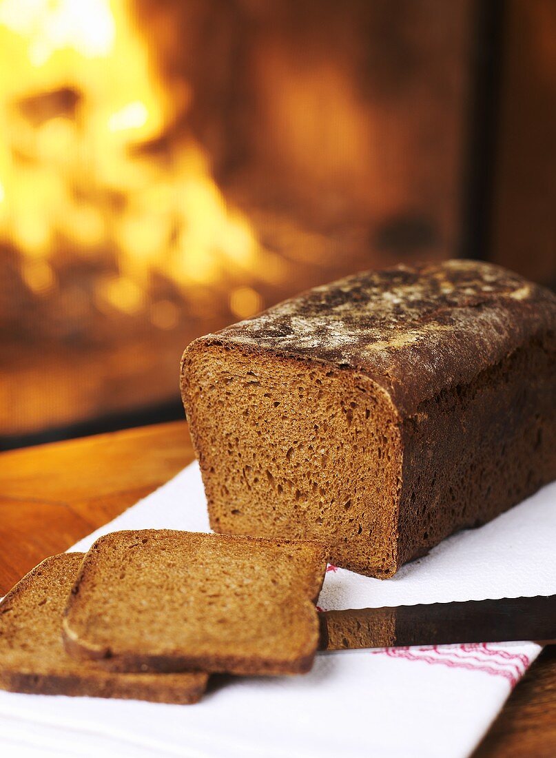 Rye bread, partly sliced, in front of open fire