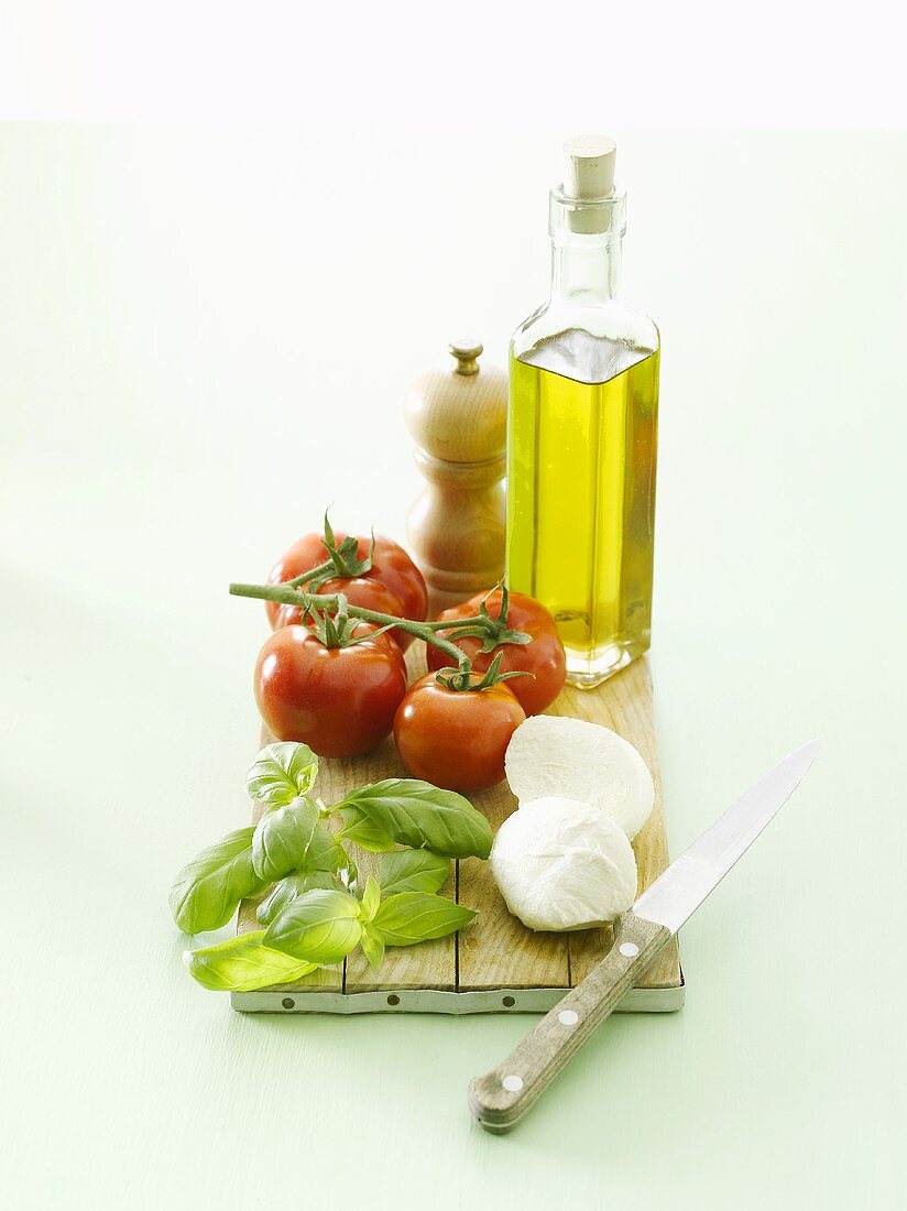 Olive oil, tomatoes, basil & mozzarella on chopping board