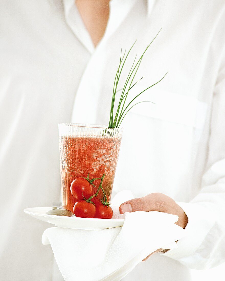 Person serviert Tomaten-Orangen-Drink (Spicy Tomato Shot)