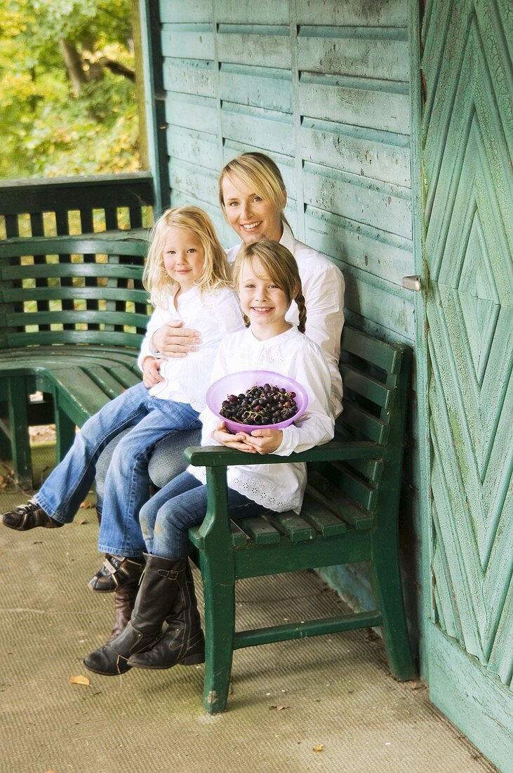 Mother and daughters on a bench outside a forest cabin