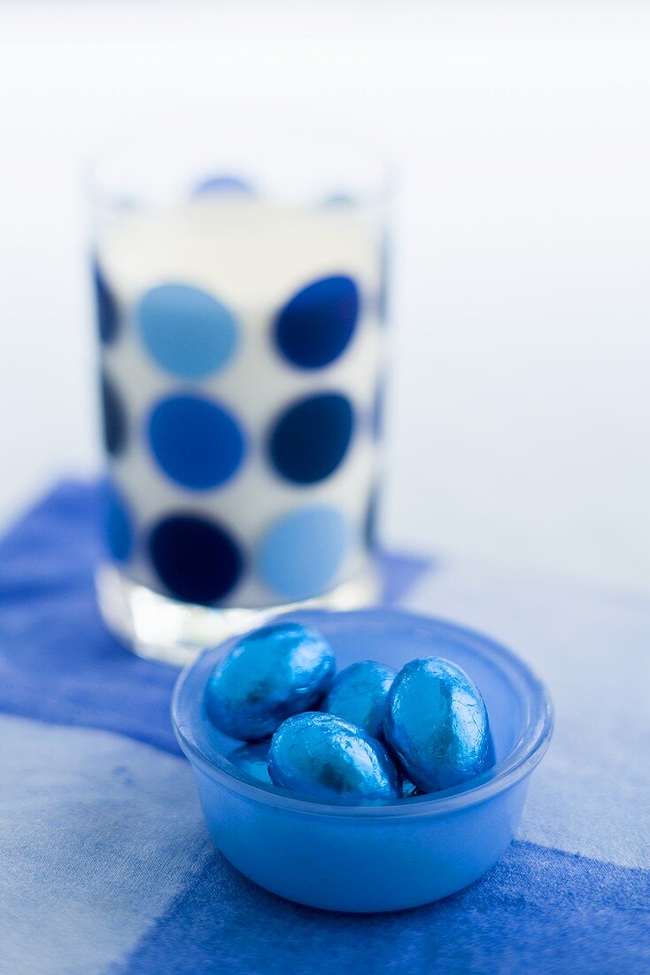 Chocolate eggs in blue foil and glass of milk