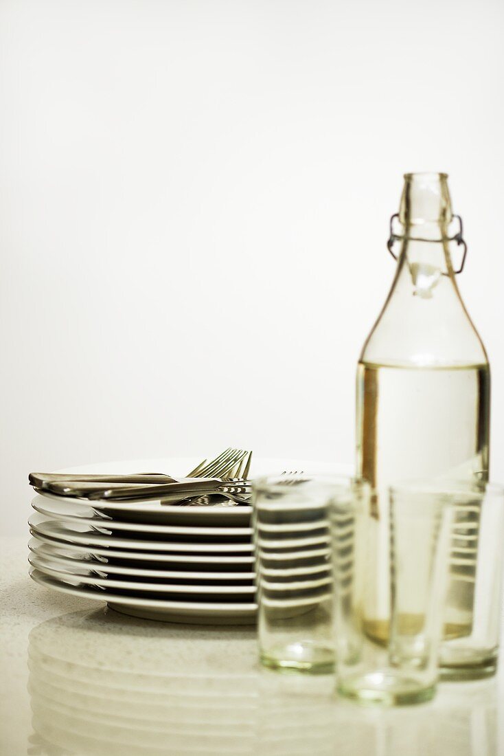 Cutlery, pile of plates, bottle of water and glasses