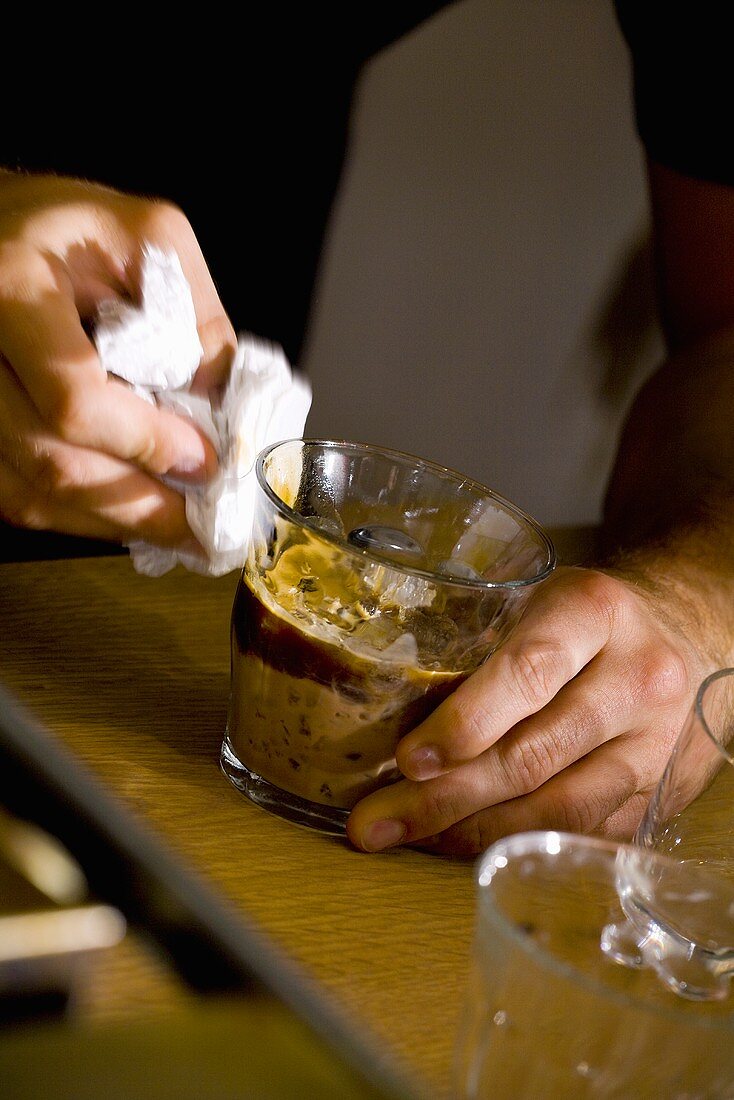 Mann wischt Glas mit Kaffee-Drink auf Eis sauber