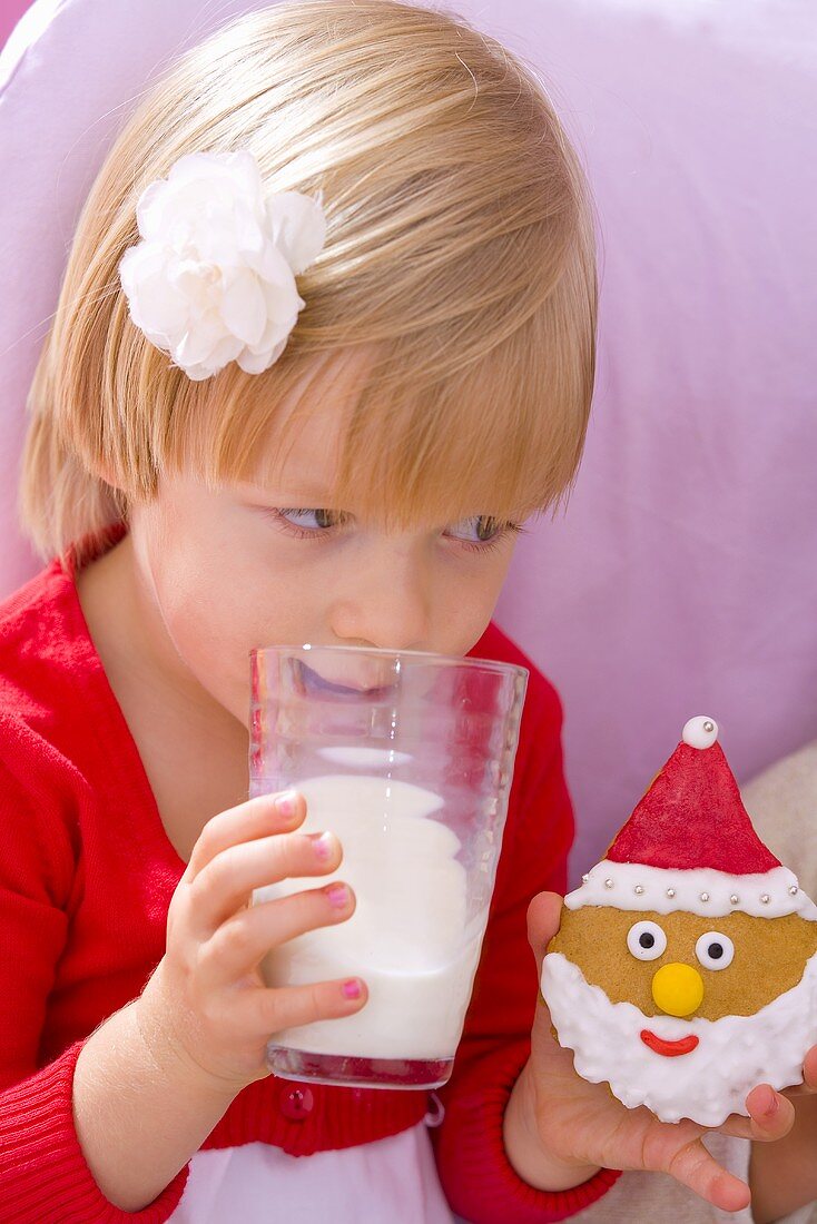Kleines Mädchen trinkt Milch und hält Keks in der Hand