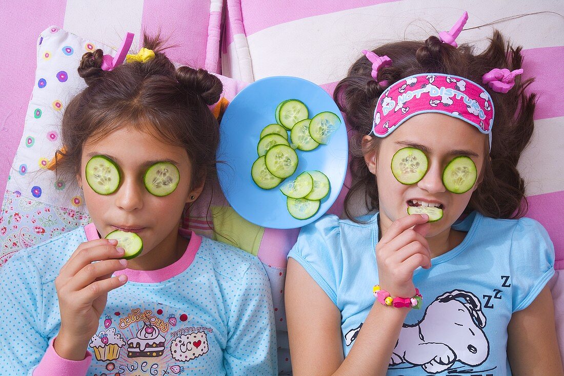Zwei Mädchen mit Gurkenmaske essen Gurkenscheiben