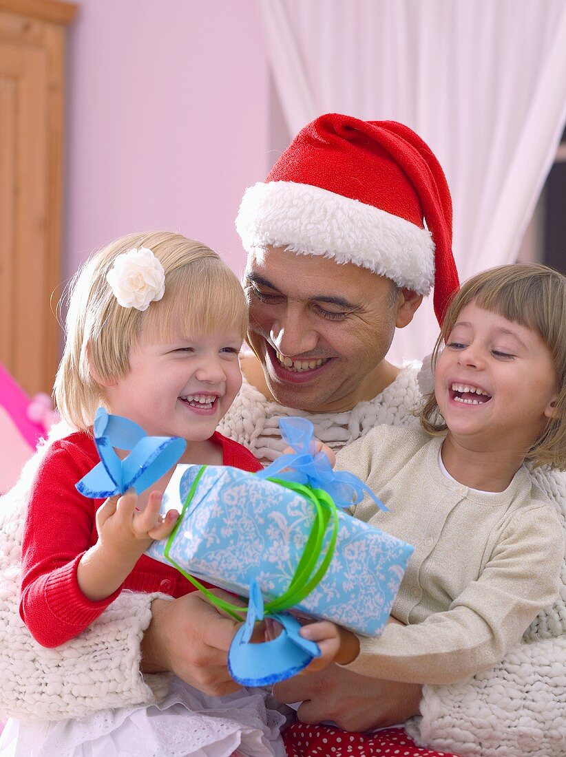 Man in Santa hat holding two girls and gift in his arms