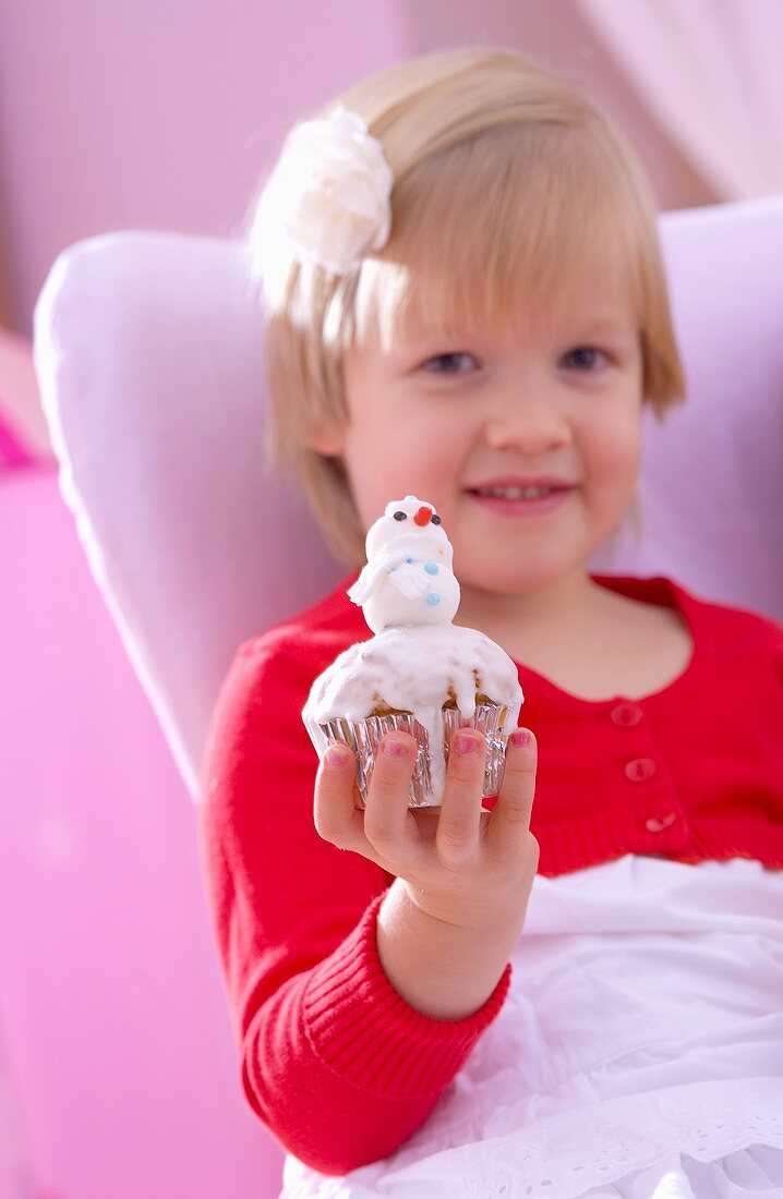 Kleines Mädchen hält Muffin mit Marzipan-Schneemann in Hand