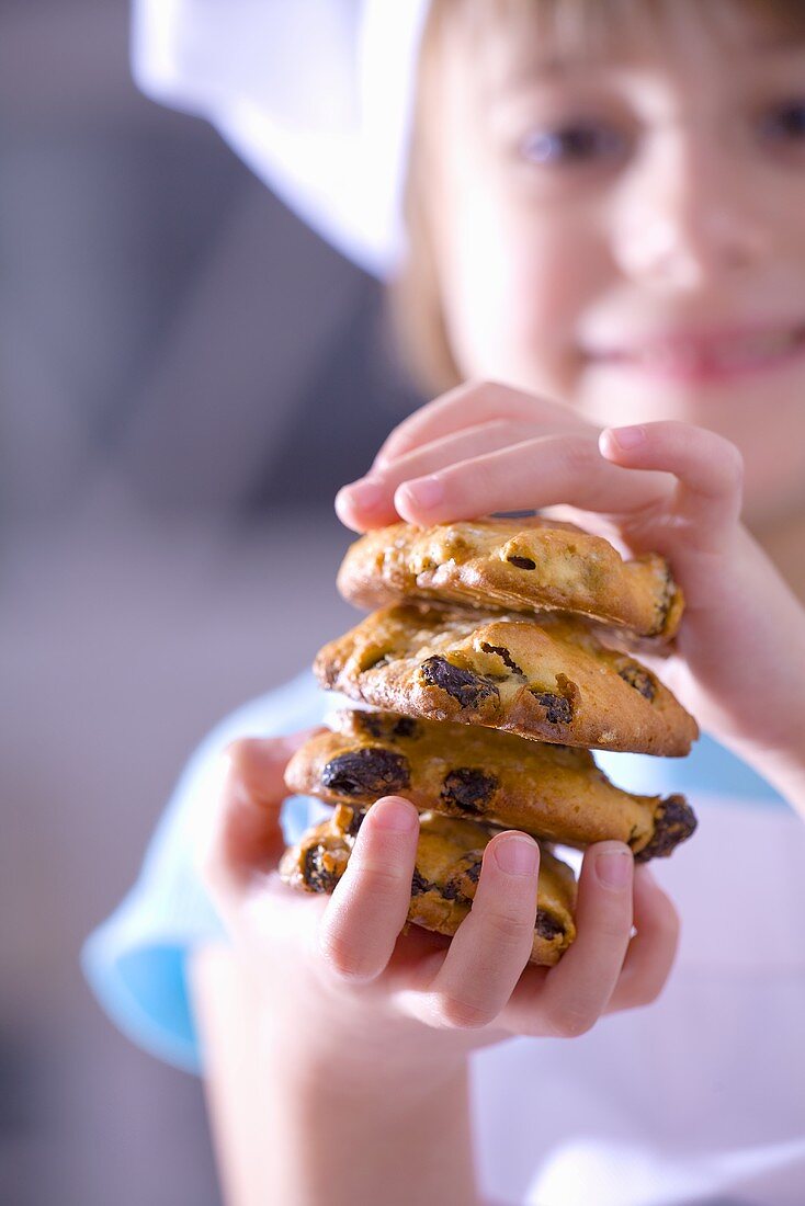 Kleines Mädchen mit Kochhaube hält Rosinen-Kekse in Händen