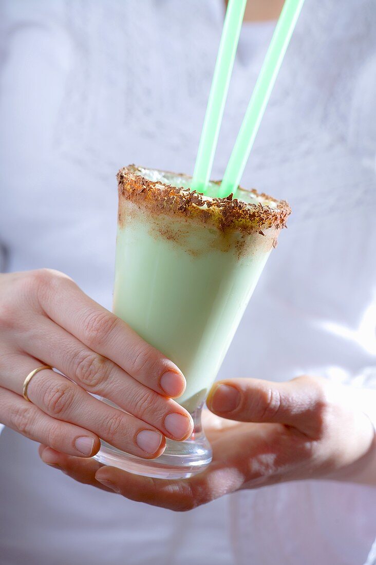 Woman holding creamy mint espresso drink in glass