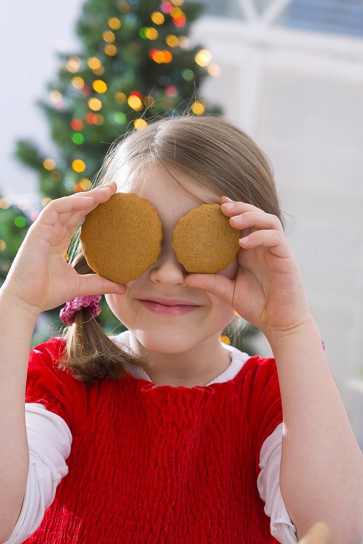 Mädchen hält sich zwei Weihnachtskekse vor die Augen