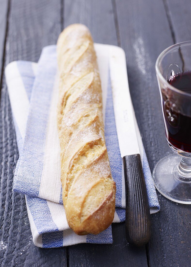 A baguette with a knife and a glass of red wine