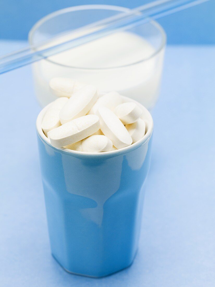 Viele Tabletten im Becher vor Glas Milch