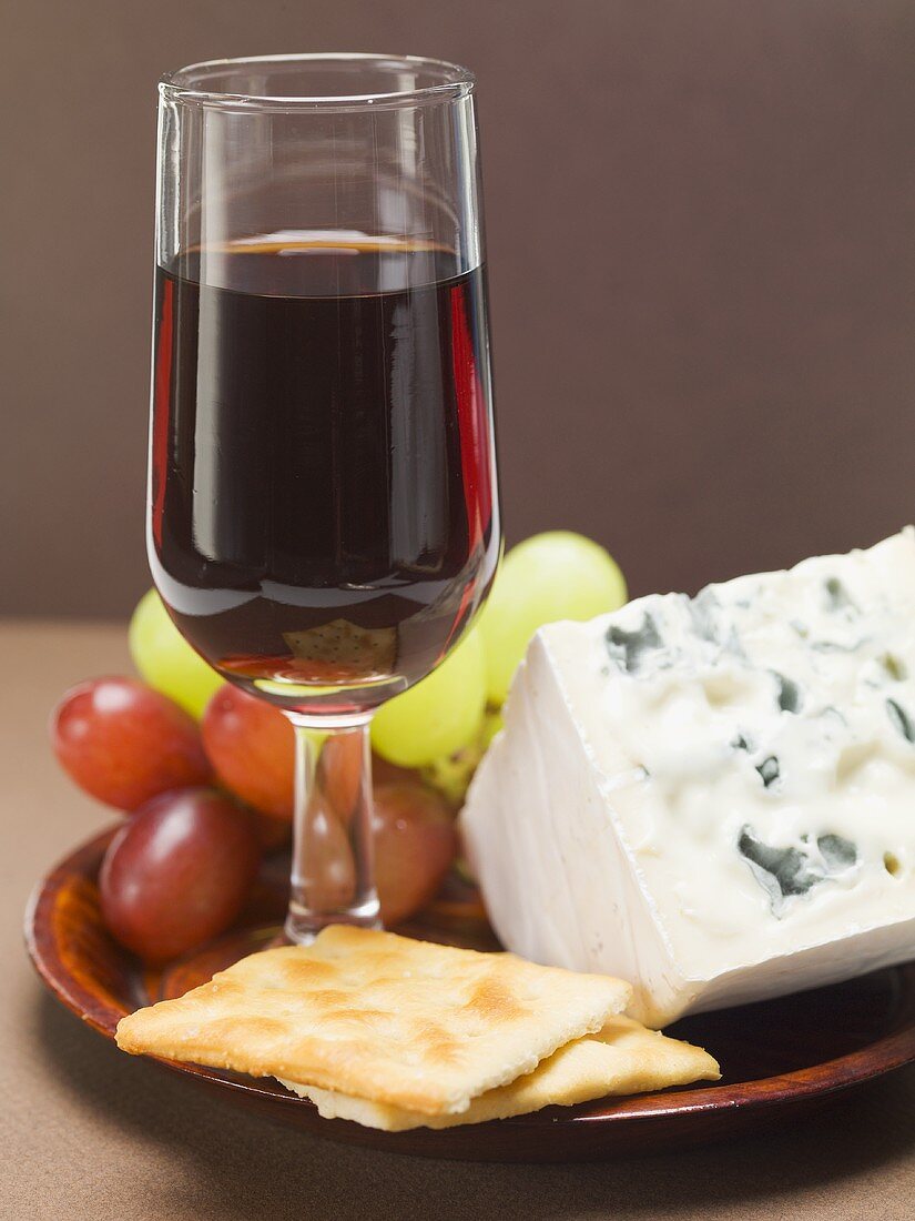 Blue cheese, crackers, grapes, glass of red wine on plate
