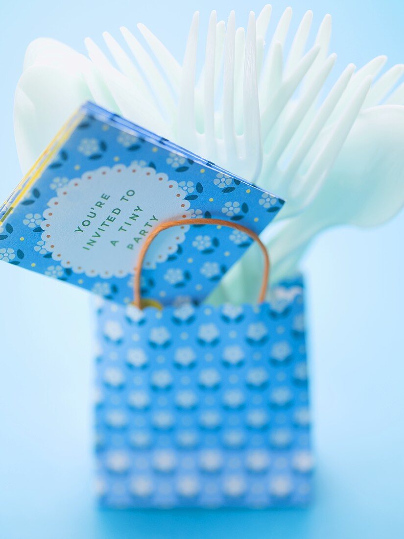 Invitation and plastic cutlery in paper carrier bag