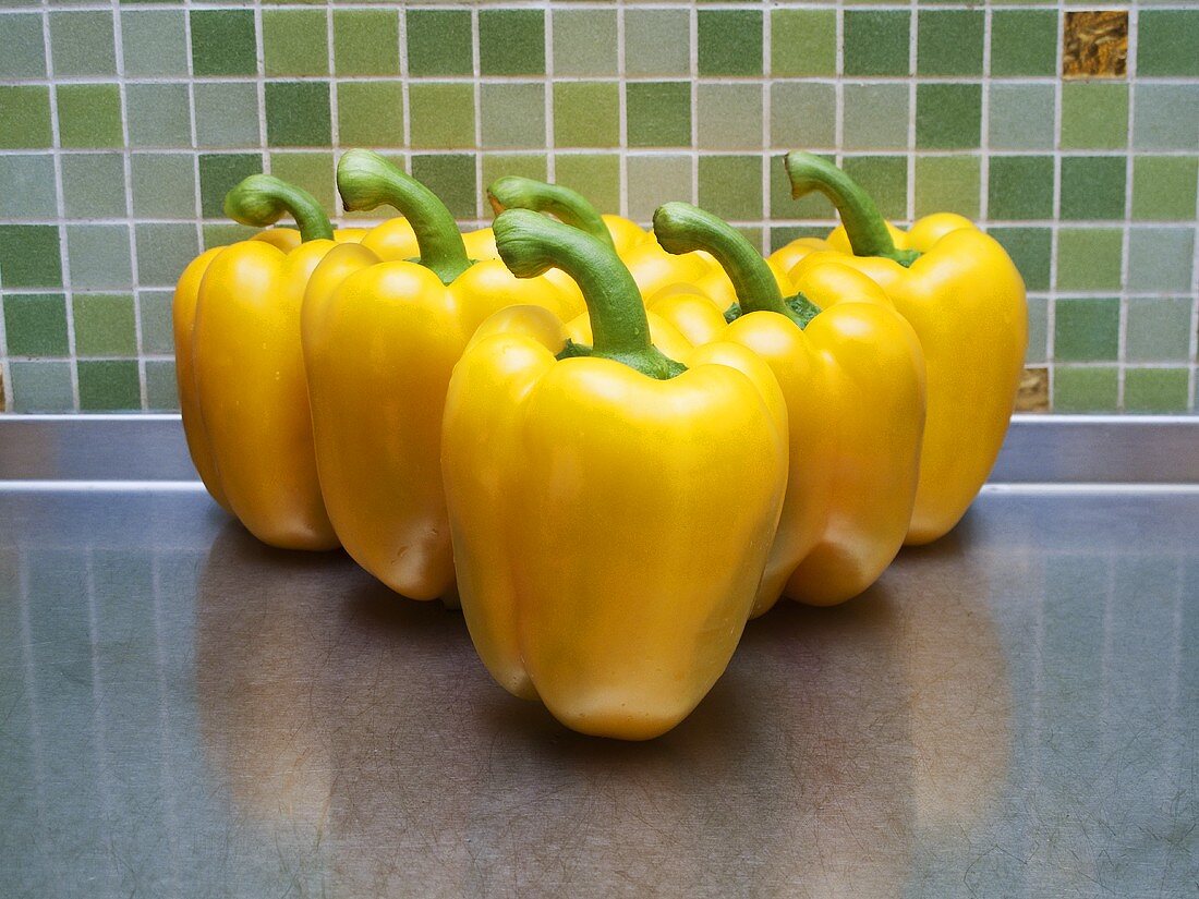 Six yellow peppers on stainless steel worktop