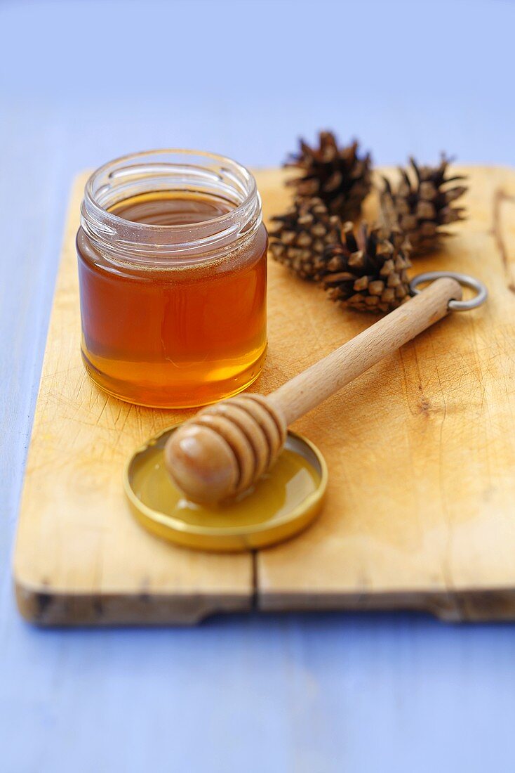 Pine honey in jar with honey dipper and pine cones