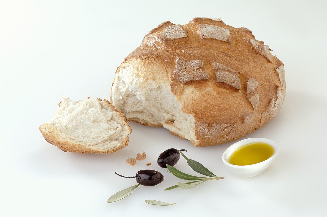 Bread baked in stone oven, a piece broken off, olive oil, olives