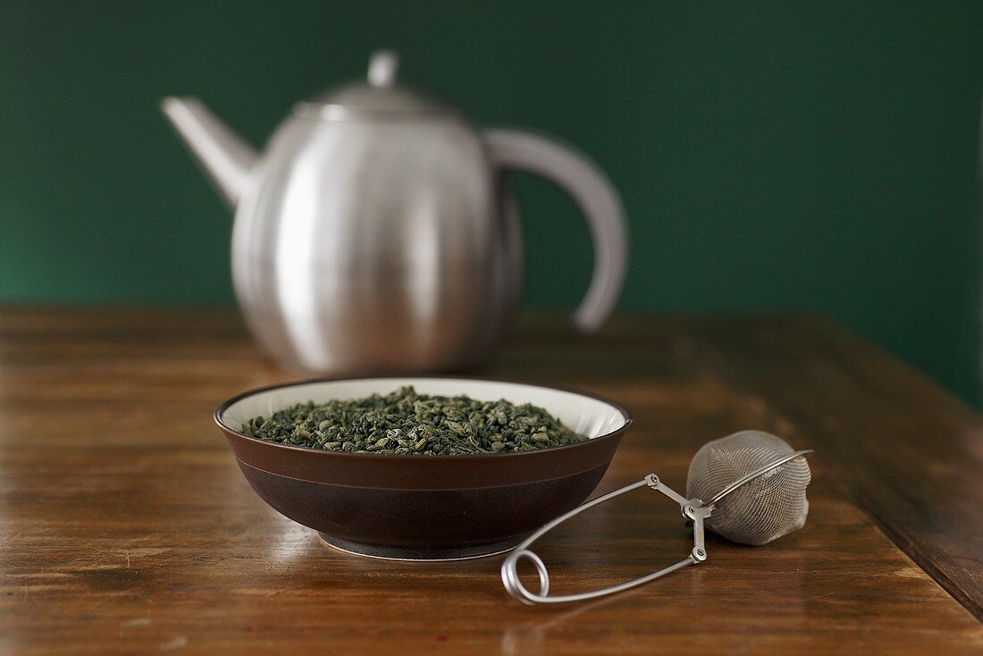 Green tea leaves, tea infuser and teapot