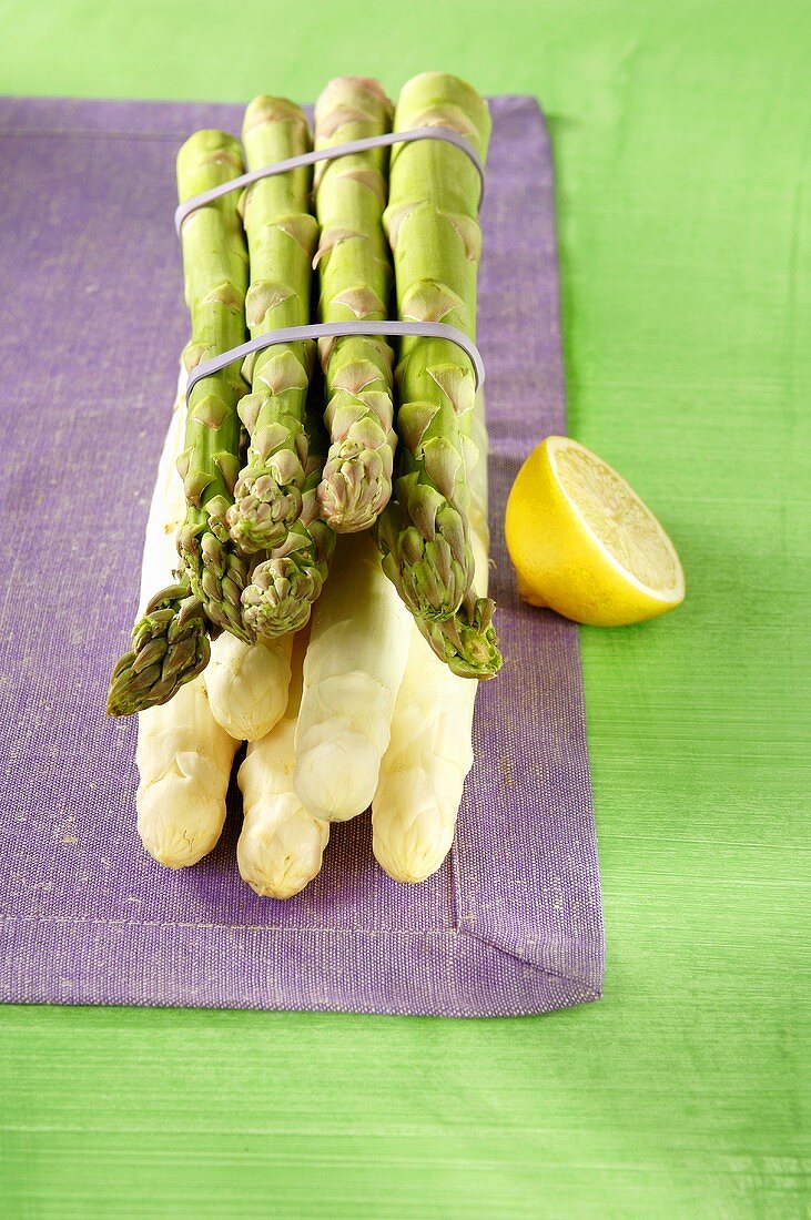 A bundle of green and white asparagus, lemon beside it